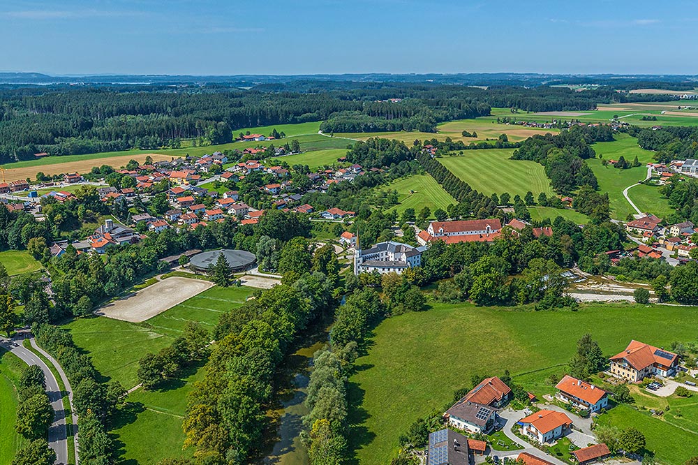 Luftbild einer ländlichen Gemeinde mit Wohnhäusern, Wiesen und Feldern in grüner Umgebung.